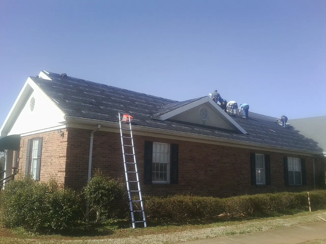 Crew tearing shingles off a brick ranch roof with a ladder set — Metal Roof Repair work by our crew in Fort Thomas