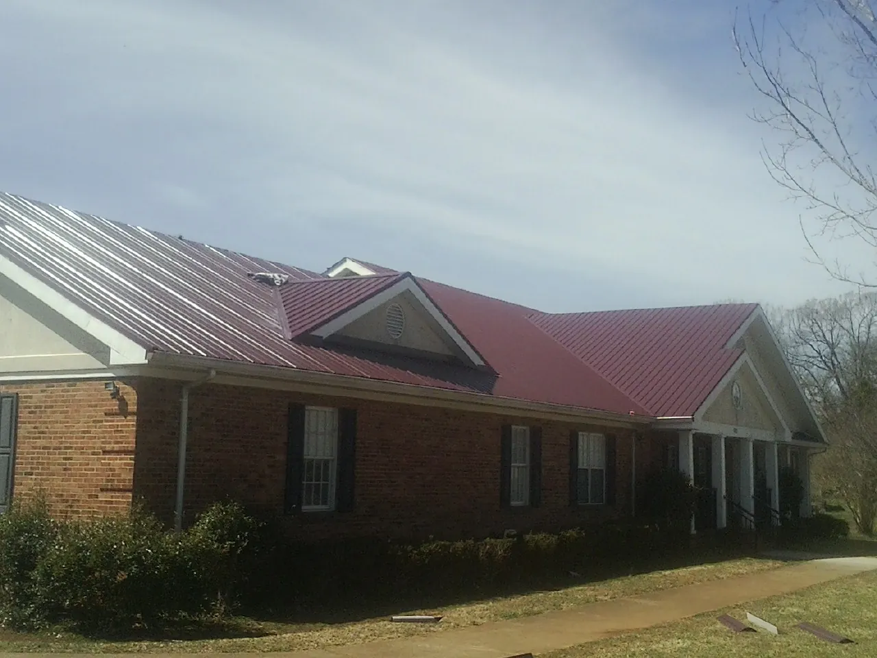Red metal roof with gabled entries on a long brick building, from a Hail Damage Roof Repair job in Fort Thomas