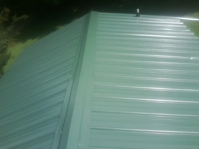 New green metal panels meeting at the ridge of a roof — Flat Roof Repair work by our crew in Fort Thomas
