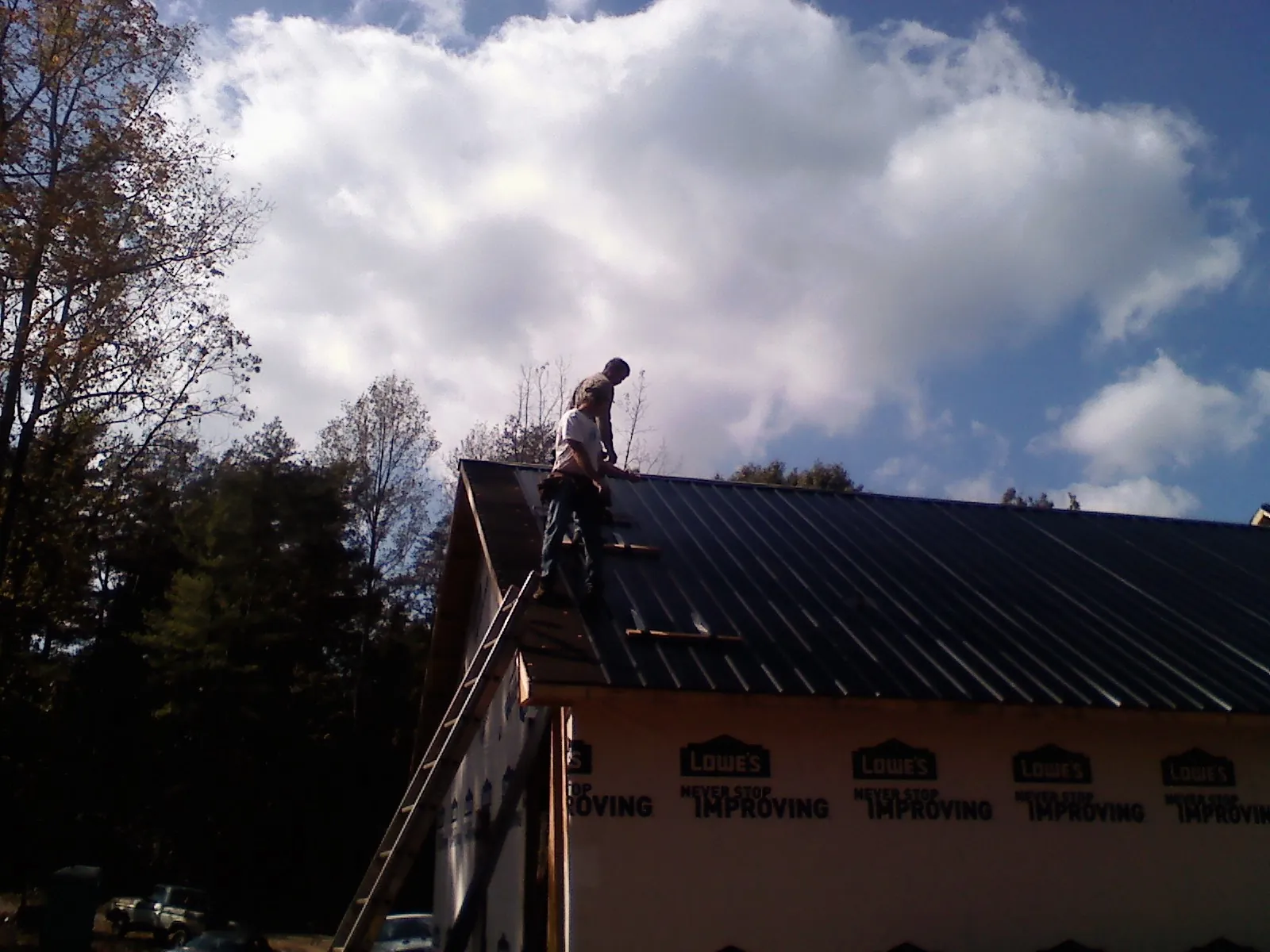 Roofer fastening dark metal panels high against a cloudy sky, from a Roof Inspection job in Fort Thomas