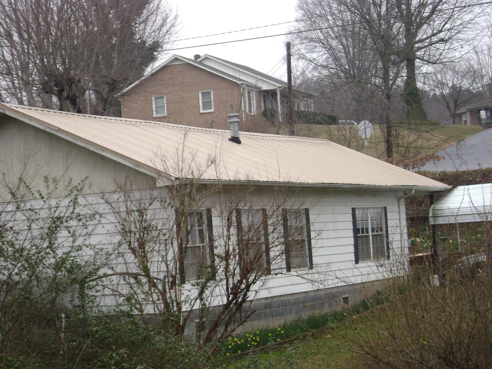Tan metal roof on a white sided house set into a hillside — Commercial Roofing by Roofing Brothers in Fort Thomas